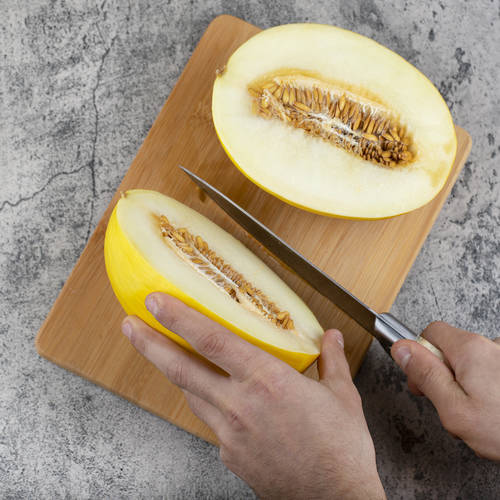Hands cutting fresh yellow melon on wooden cutting board