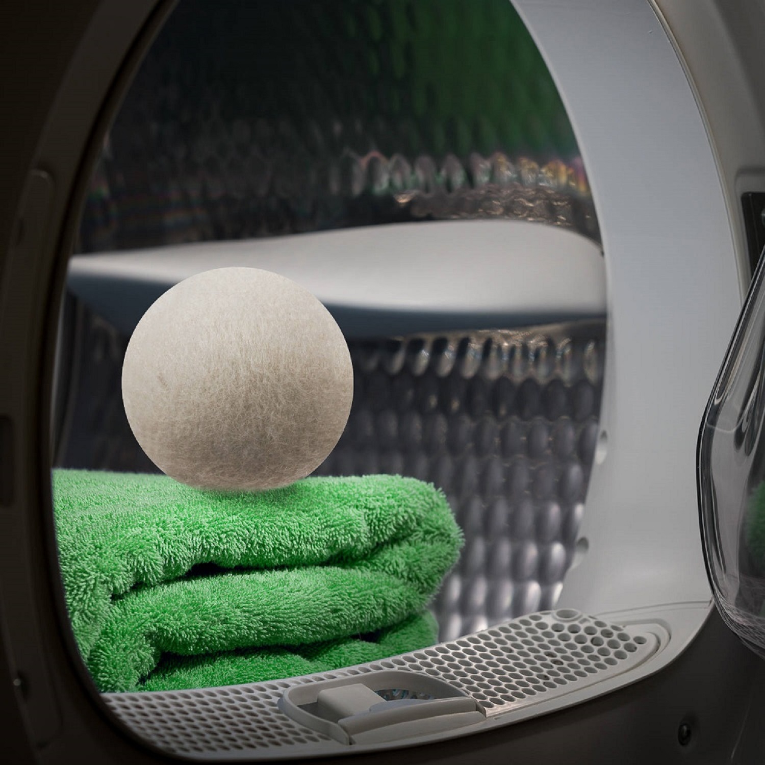 Dryer with open door in a dark room. Green towels are stacked inside the drum.