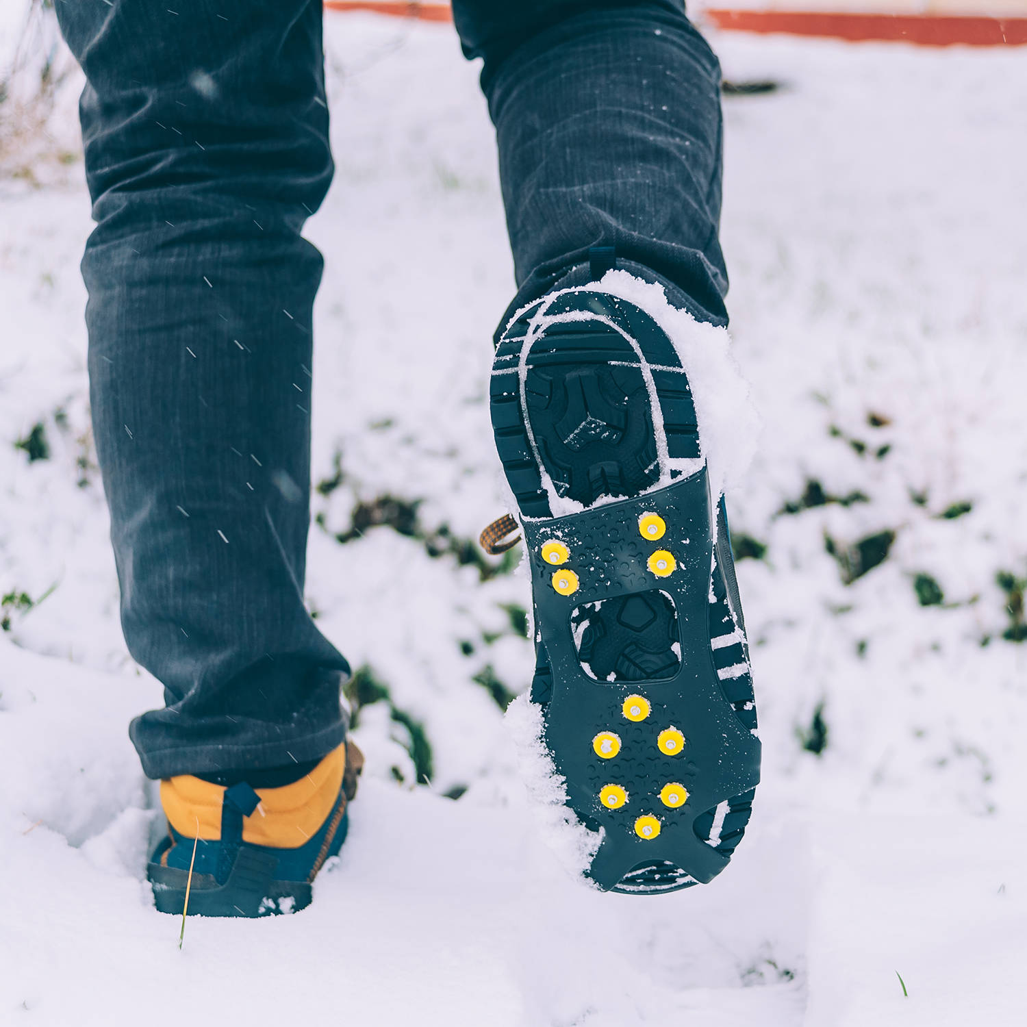 The man has ice shoes on his shoes. A people walks in the snow in winter.