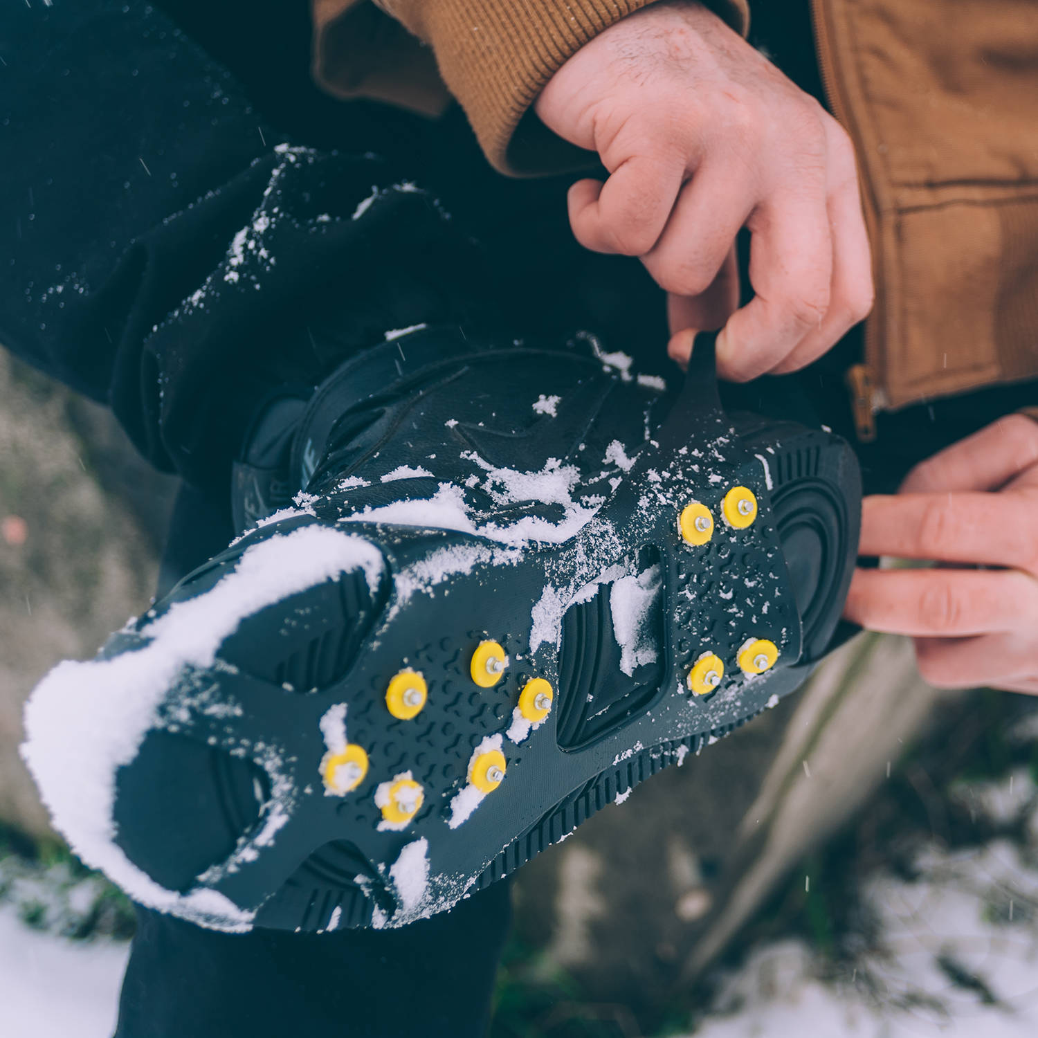 The man has ice shoes on his shoes. A people walks in the snow in winter.