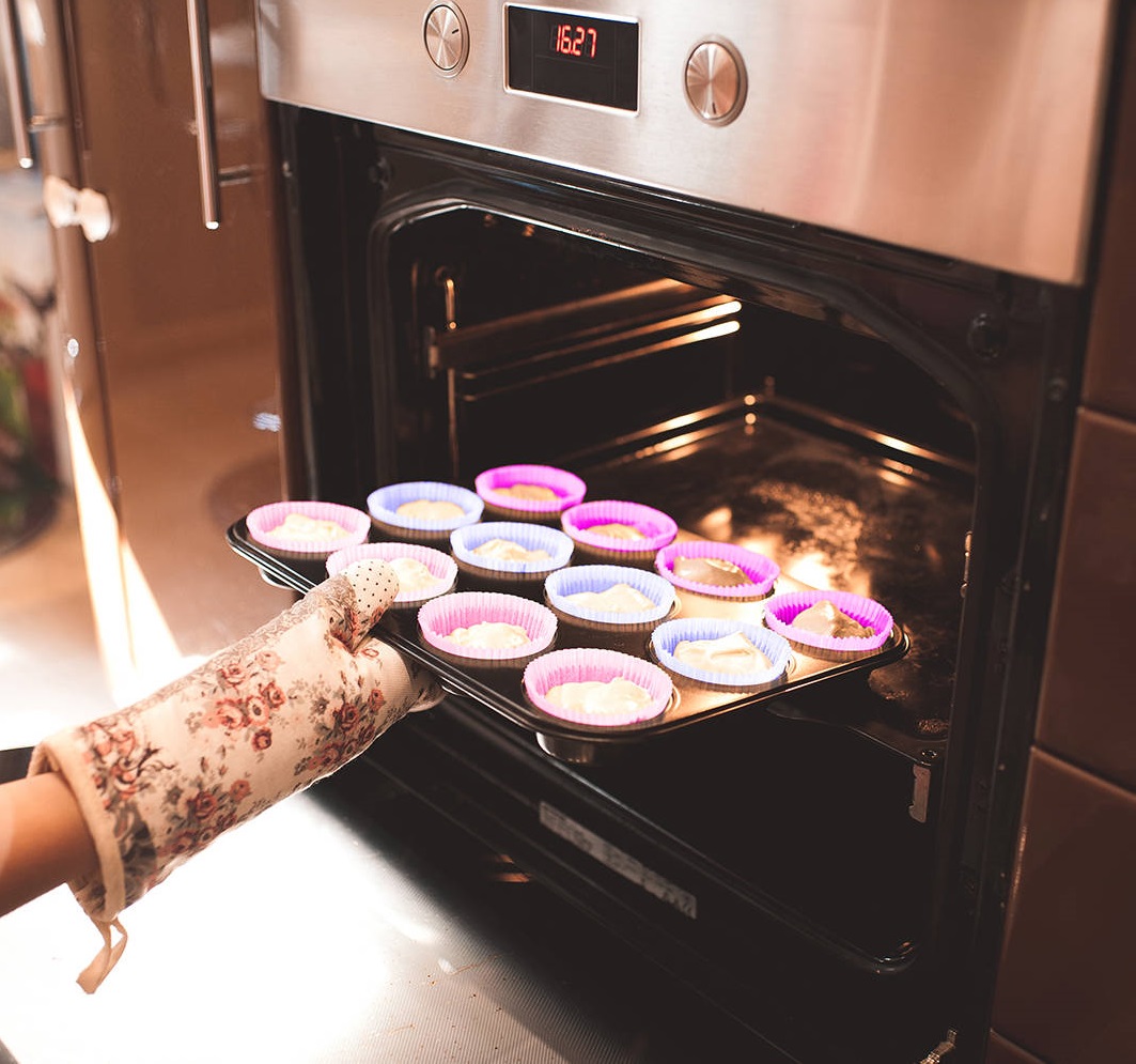 Woman put batter for cupcakes in oven in kitchen closeup. Cooking time.